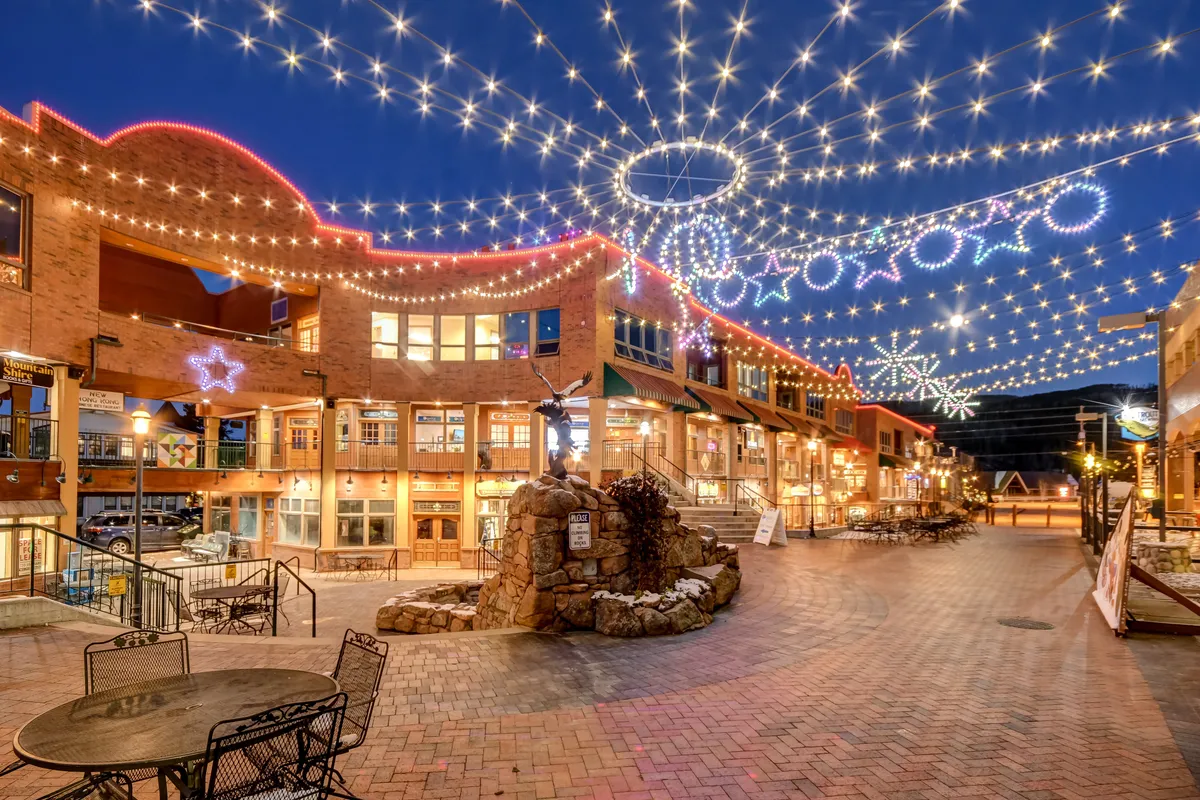 A festive outdoor scene with string lights, decorative stars, a bubbling fountain, inviting seating, and storefronts. The space feels lively and welcoming, ideal for evening gatherings, socializing, and enjoying the vibrant atmosphere of downtown Winter Park.