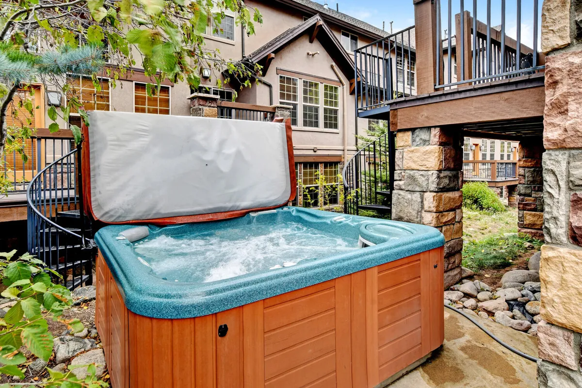 This image showcases a spacious outdoor hot tub set against lush greenery and crafted stone architecture. The setting is tranquil, with seating space for several people, inviting guests to relax and unwind while enjoying the natural surroundings. The scene captures the feeling of a refreshing soak after a day spent outdoors, with the promise of sunset views over the mountains.