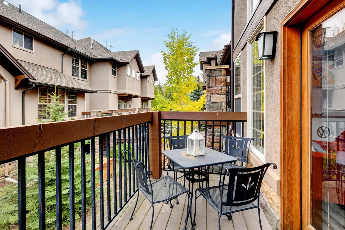 A cozy exterior balcony with a table, lantern, and trees in the background, inviting guests to enjoy a quiet morning coffee or an intimate gathering surrounded by alpine scenery.
