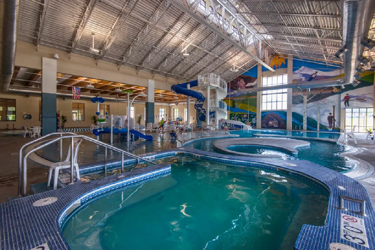 A vibrant indoor recreation facility showing water slides, pools, colorful murals, and lounging areas—a lively, family-friendly environment.