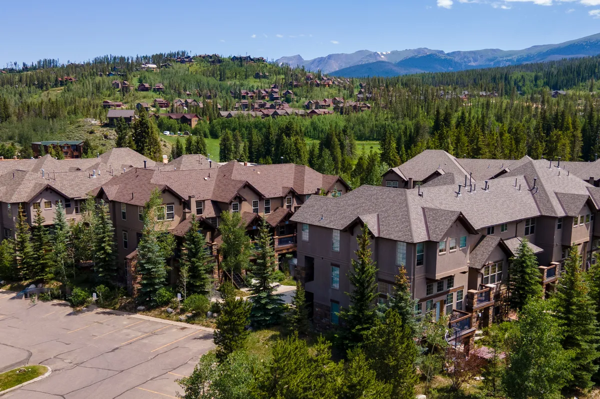A broad view of a cluster of townhomes nestled among trees with a stunning mountain backdrop. The image conveys a sense of community, space, and access to outdoor adventures, capturing the broader environment where the property is located.