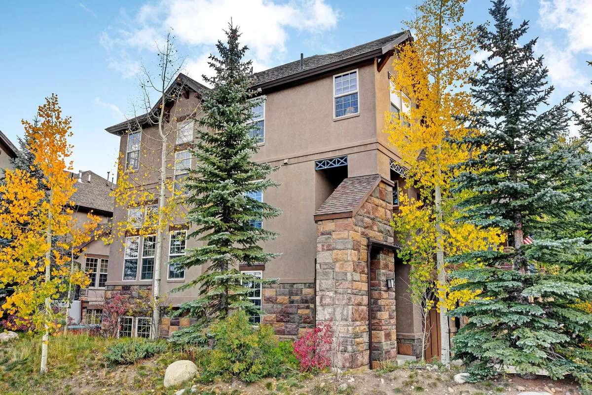 An inviting exterior scene showcasing a stone entrance surrounded by tall trees and vibrant, colorful foliage. The area exudes a welcoming atmosphere and hints at nearby trails and nature, perfect for family outings and exploration.