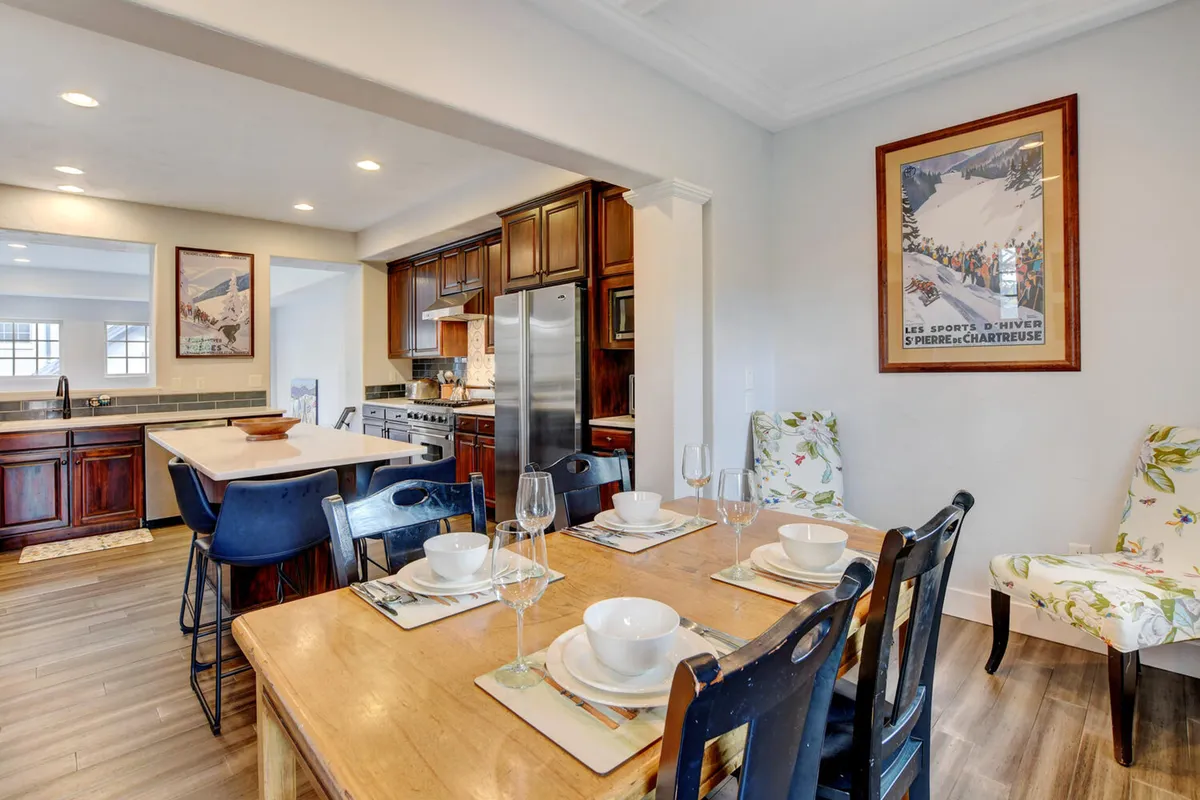 A dining area set for a meal, featuring a kitchen island in the background, floral-patterned chairs, and a decorative poster. The table is ready for gatherings—reflecting the warmth of family meals and casual conversations.