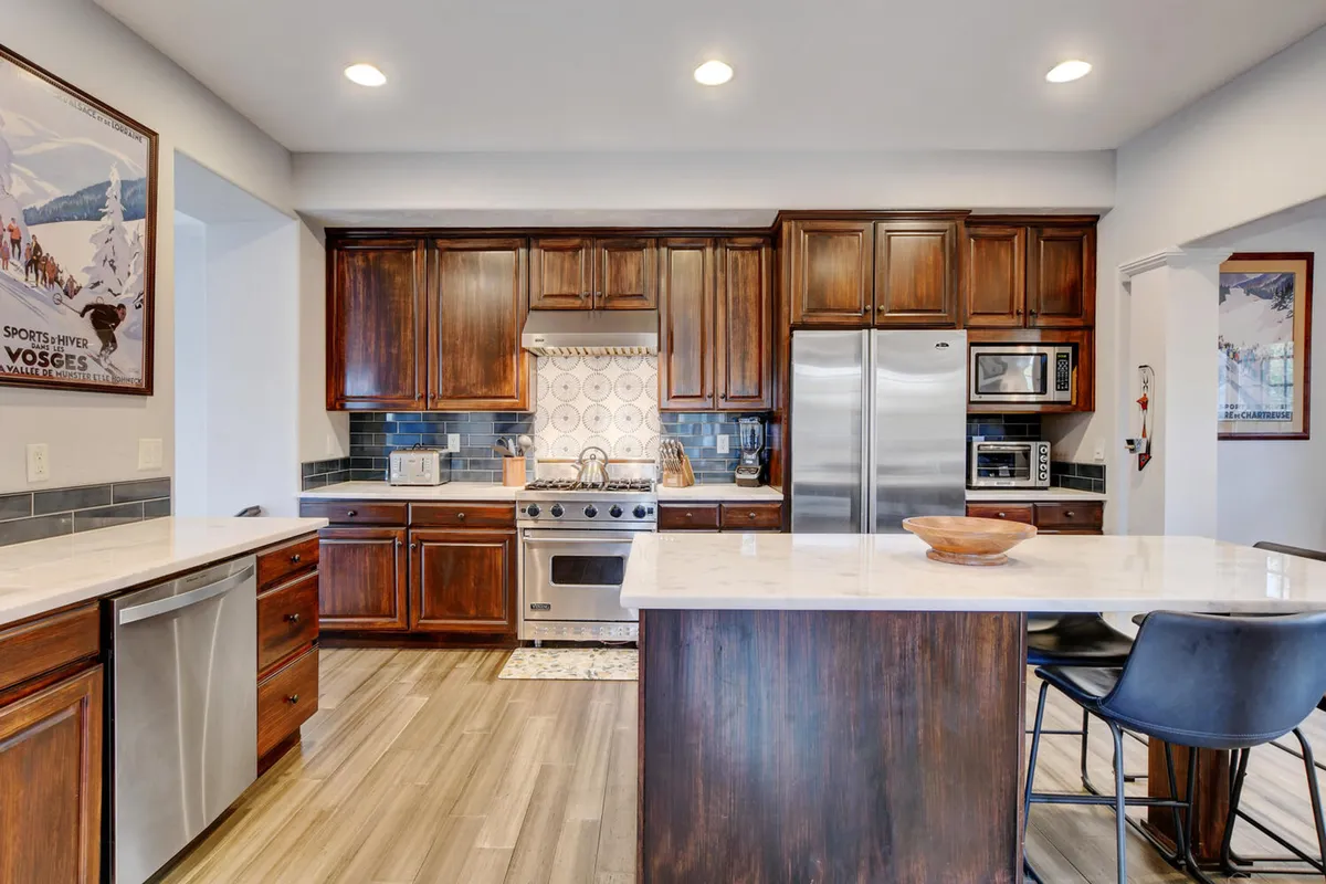 A stylish kitchen featuring a central island, high-end stainless steel appliances, including a prominent Viking range, and rich wood cabinetry. The decorative backsplash adds flair, while the layout encourages culinary creativity and social interaction.