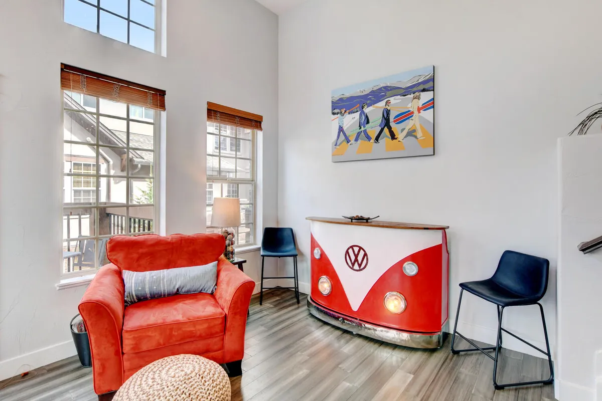 A playful interior shot centered on the custom Volkswagen Bus bar, with a vibrant red armchair and colorful artwork adding personality to the space. The scene captures a sense of fun, relaxation, and the unique focal point the bar brings to the home.